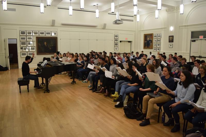 Jeff Douma sits at piano while directing seated members of Yale Glee Club
