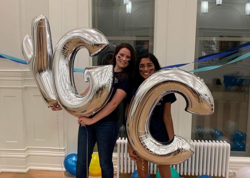 Image of two members of the Glee Club smiling and holding oversized silver balloons spelling YGC